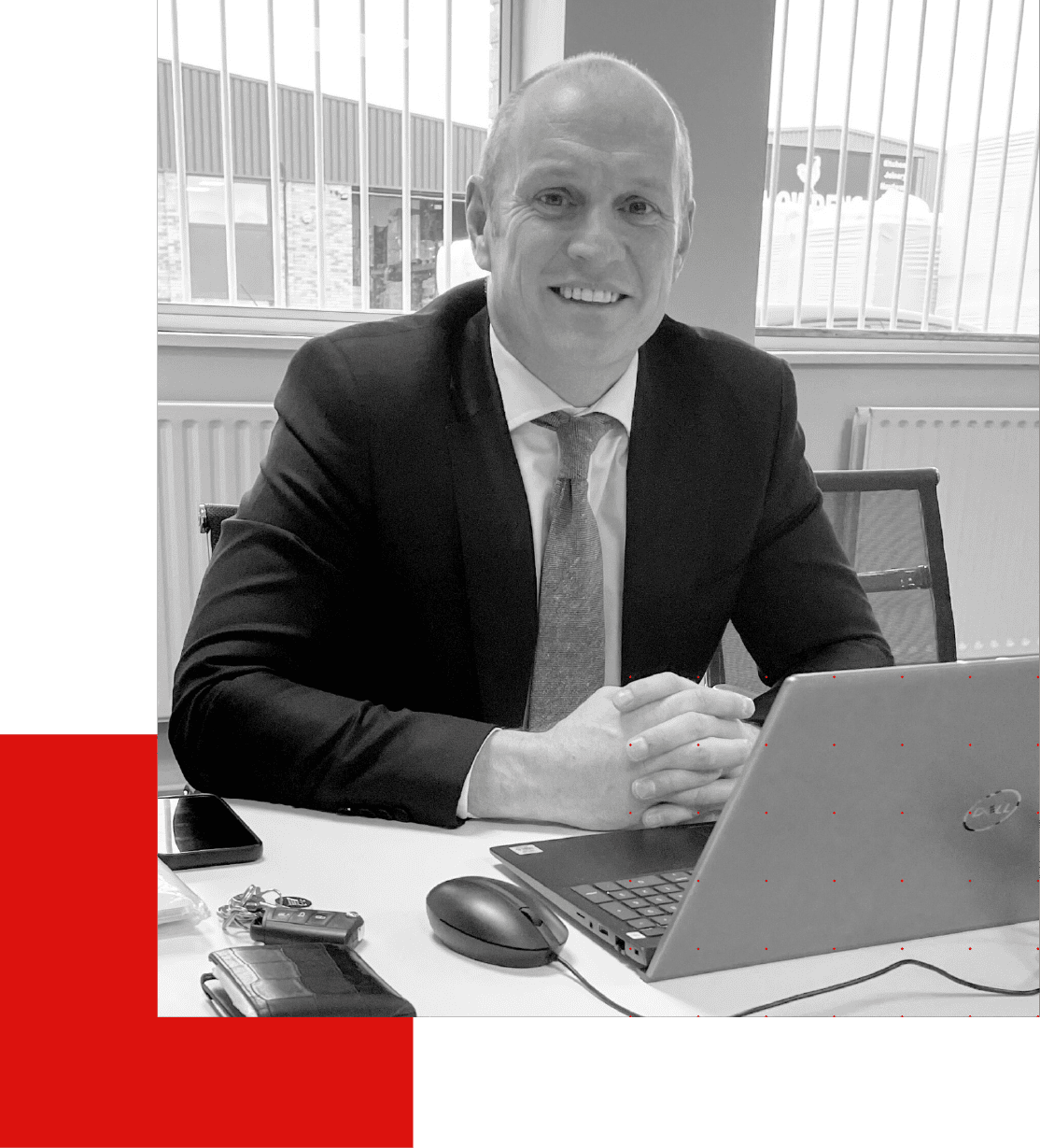 Smiling man in suit at desk with laptop and phone.