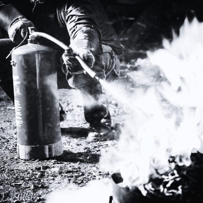 Fire test Person using fire extinguisher on outdoor flames amid smoke.