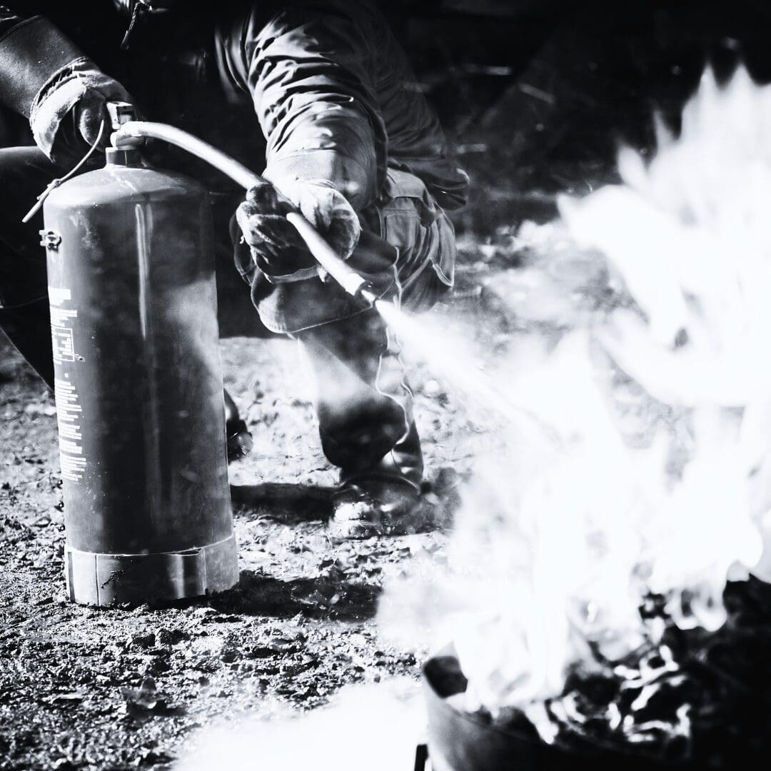 Person using fire extinguisher on outdoor flames amid smoke.