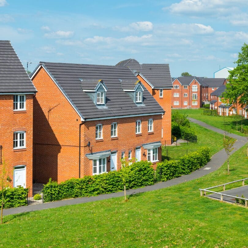 Modern brick houses with gardens and a grassy path on a sunny day.